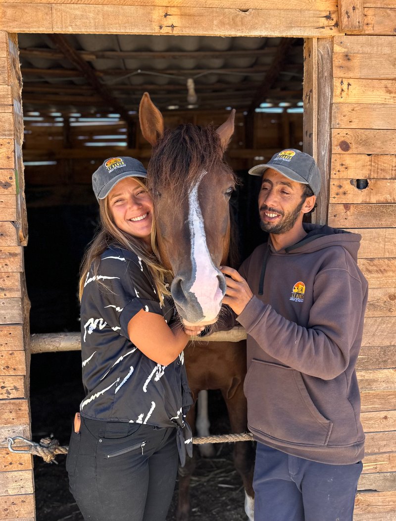 Sarah and Mohamed Bicha smiling with a horse in the stables of Ranch des Dunes